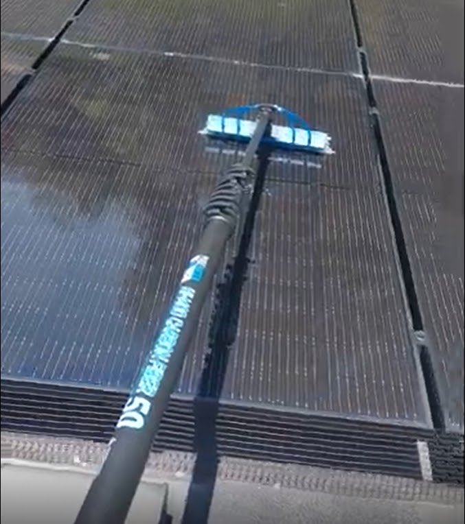 Soft water-fed brush cleaning a row of rooftop solar panels
